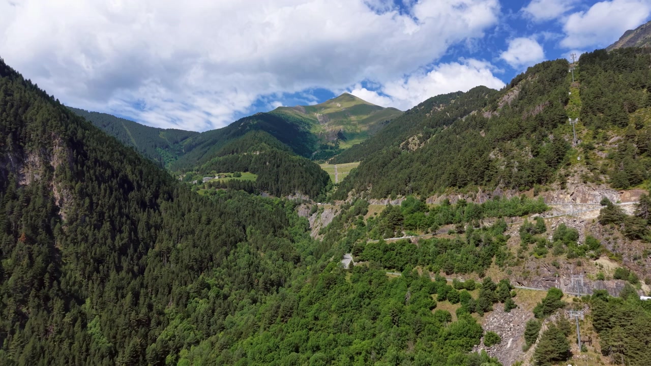 Lussureggiante valle di montagna verde in Andorra con fitte foreste di pini, strada tortuosa, pendii rocciosi e nuvole drammatiche sulle cime dei Pirenei in estate.