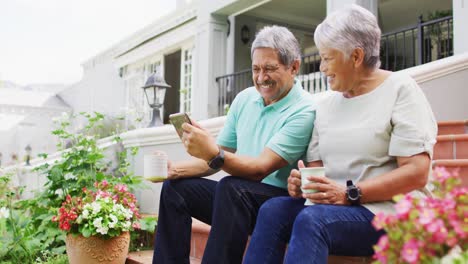 video de una feliz pareja de ancianos biraciales usando una tableta en el jardín