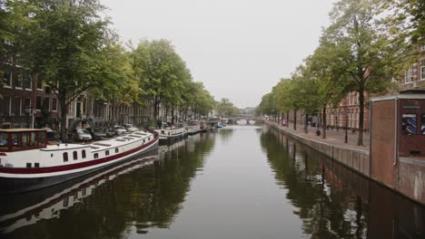 pan of beautiful canal in amsterdam with houseboats docked at the quay