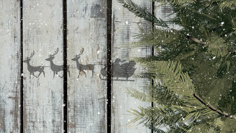 tree branches and santa claus in sleigh being pulled by reindeers against wooden plank