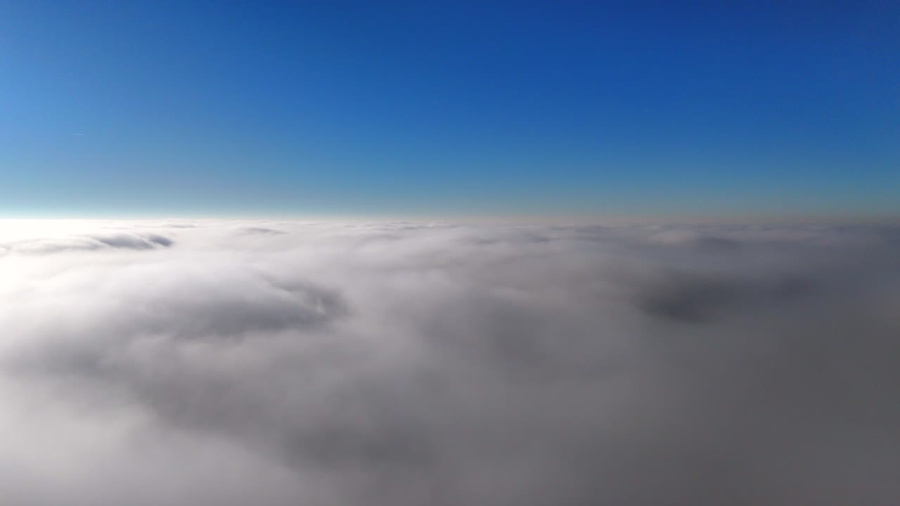 Sunny day above clouds with blue sky. Cinematic drone flight over white cloudscape in America. Forward aerial wide shot.