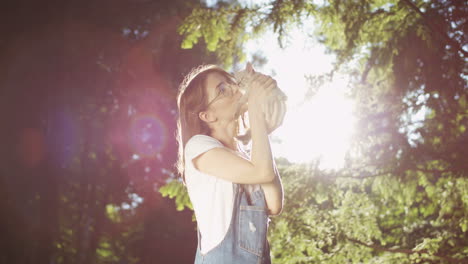 young caucasian woman in glasses holding small cat and kissing it in the park on a summer day