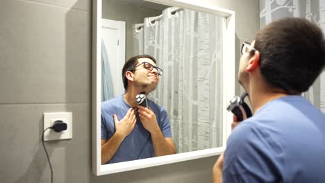 Young-man-shaving-beard-hair-on-chin-in-bathroom,-mirror-reflection