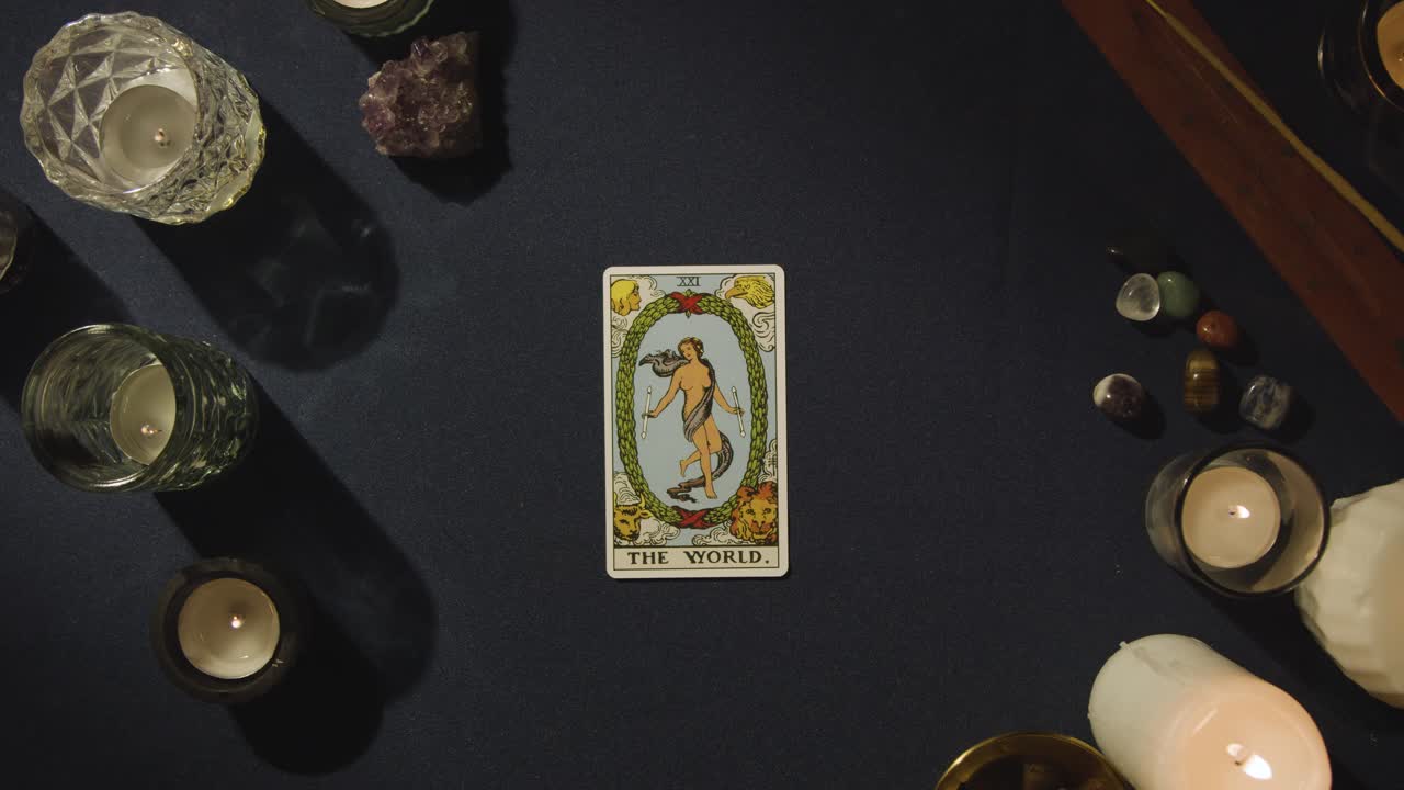toma aérea de una persona que da una lectura de cartas del tarot colocando la carta del mundo en la mesa
