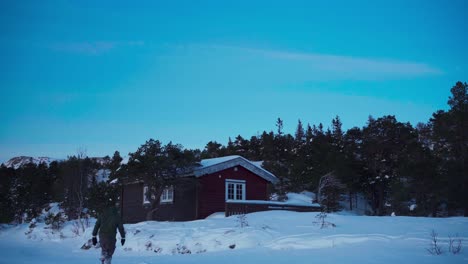 a man strides toward the wooden cabin nestled in the snowy landscape in bessaker, trondelag county, norway - static shot