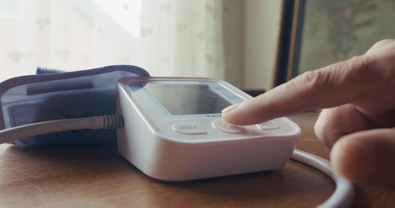 Side view close up of a home patient pressing the power button on a digital blood pressure monitor. Captures daily health tracking, hypertension checks, and personal healthcare routines.