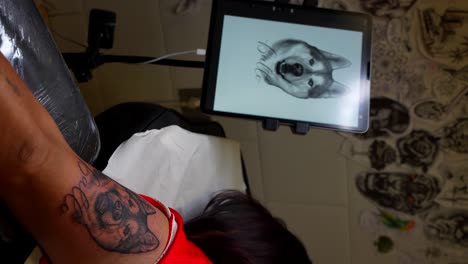fresh dog face tattoo on a woman's arm with the design displayed on a tablet screen in a studio. vertical