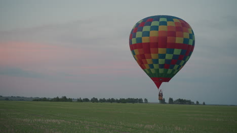 passengers flying in colorful hot air balloon basket above expansive green field at sunset sky with burner flame bursts and gentle breeze framing tranquil aerial adventure