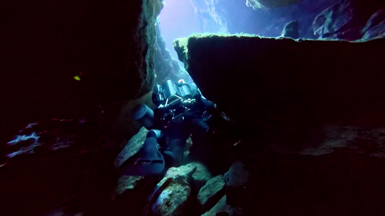 Deep blue light illuminates a brave technical cave diver navigating through a narrow limestone tunnel squeeze underwater during a summer exploration mission a dark subterranean aquatic cavern system