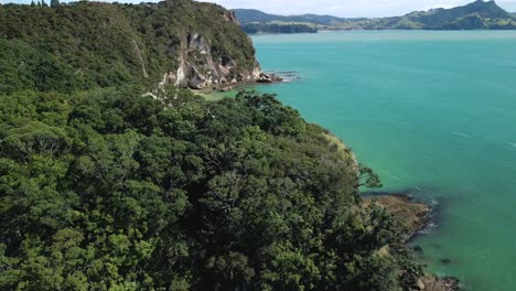 Drone-rising-over-scenic-clifftops-at-low-tide-in-New-Zealand-with-mountain-backdrop