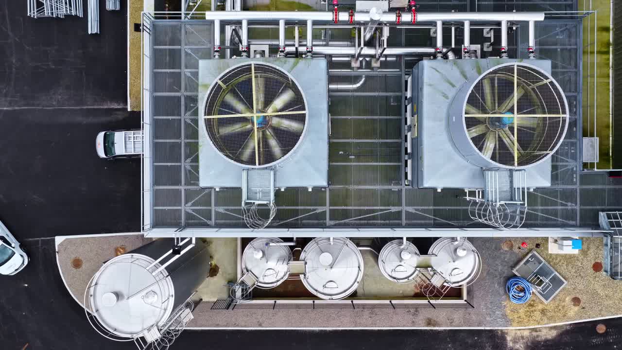 Aerial view of large HVAC cooling fans on a roof and steel tanks