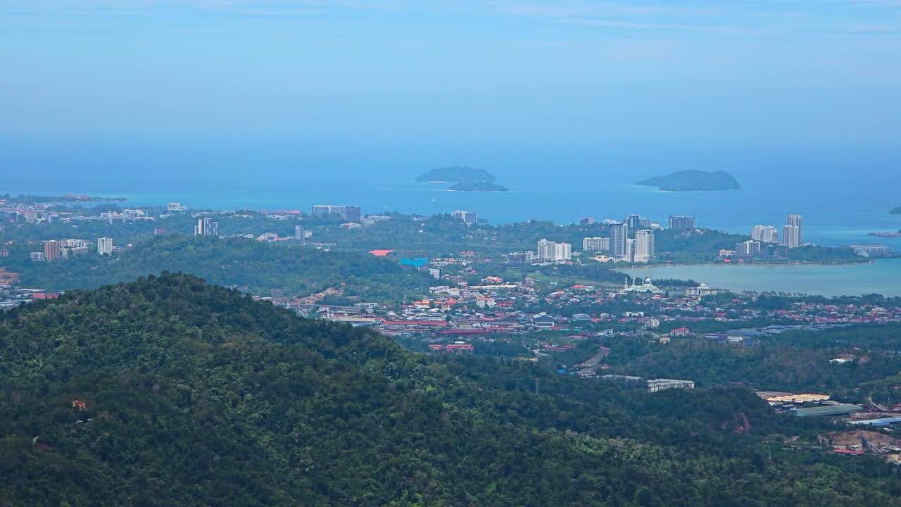 Aerial view of Kota Kinabalu from Kokol Hill showcasing lush greenery, scattered houses, and the distant coastline under a bright blue sky - telephoto zoom