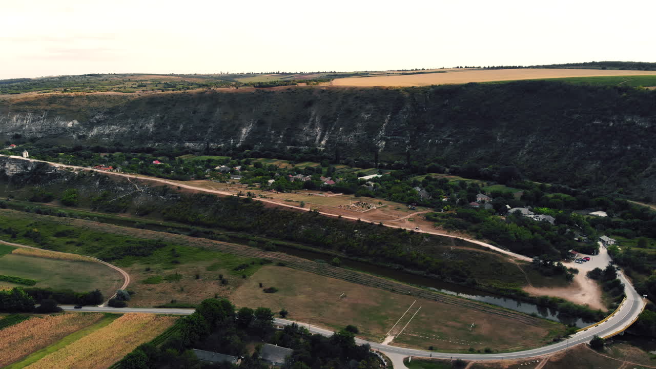 Aerial view of a winding river cutting through farmlands and a small rural village at the base of cliffs