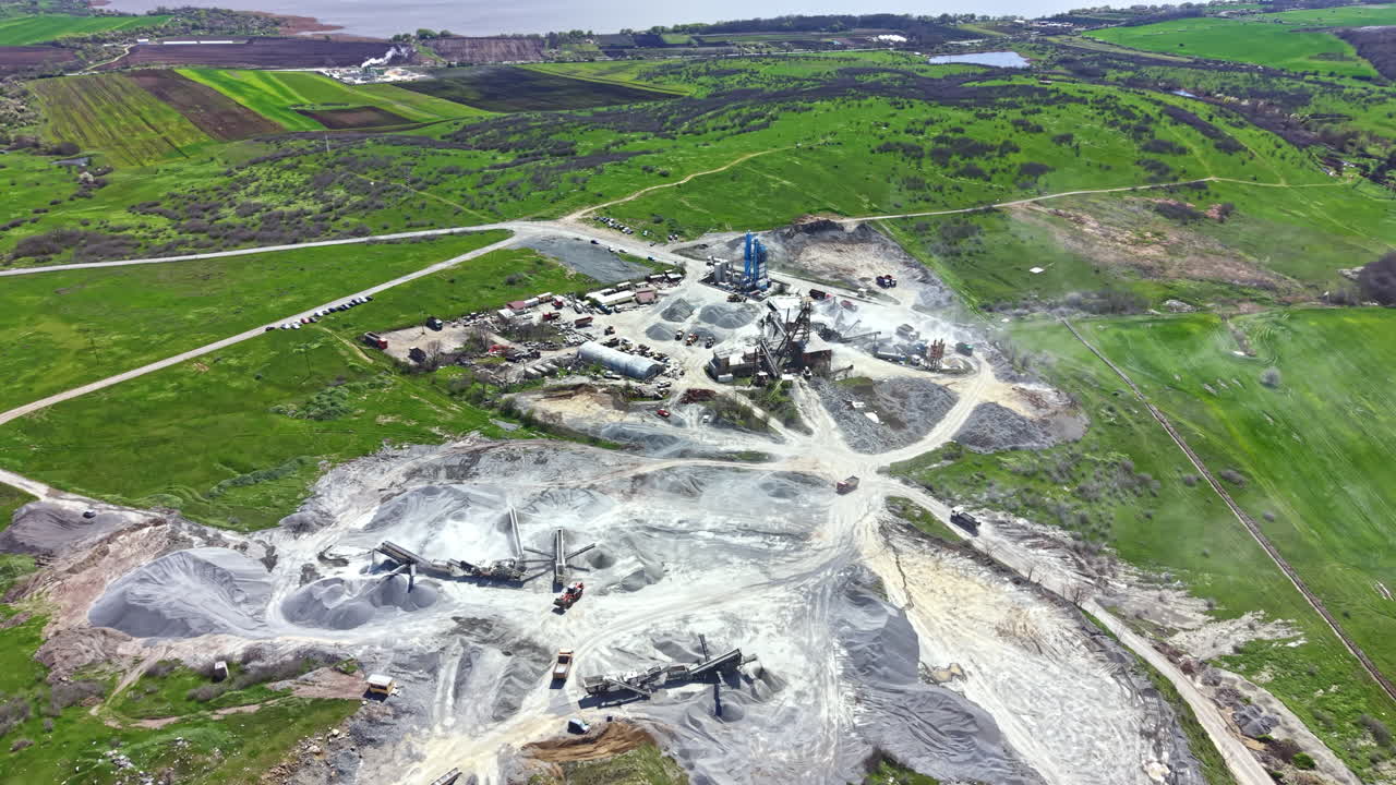 Sito di cava di granito che mostra macchinari e paesaggio durante il giorno con campi verdi e cieli sereni.