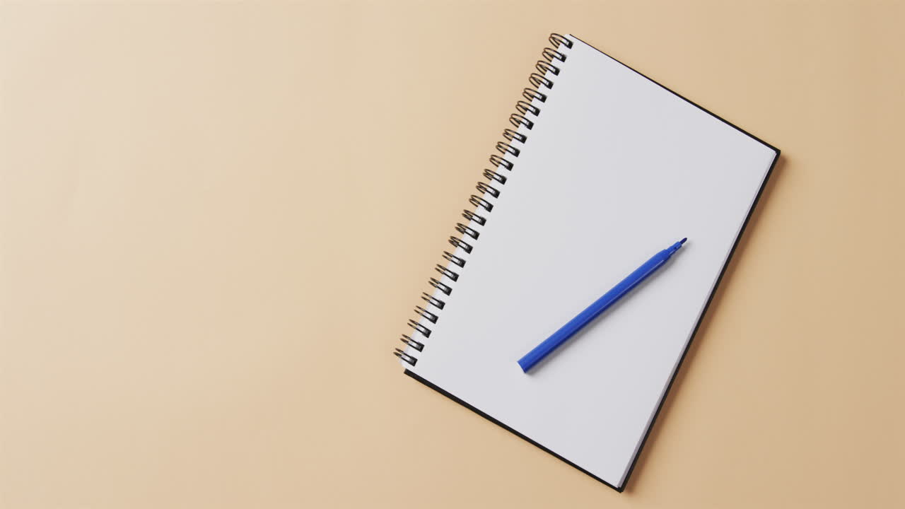 Overhead view of blue marker on notebook with copy space on beige background, in slow motion