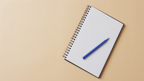 overhead view of blue marker on notebook with copy space on beige background, in slow motion