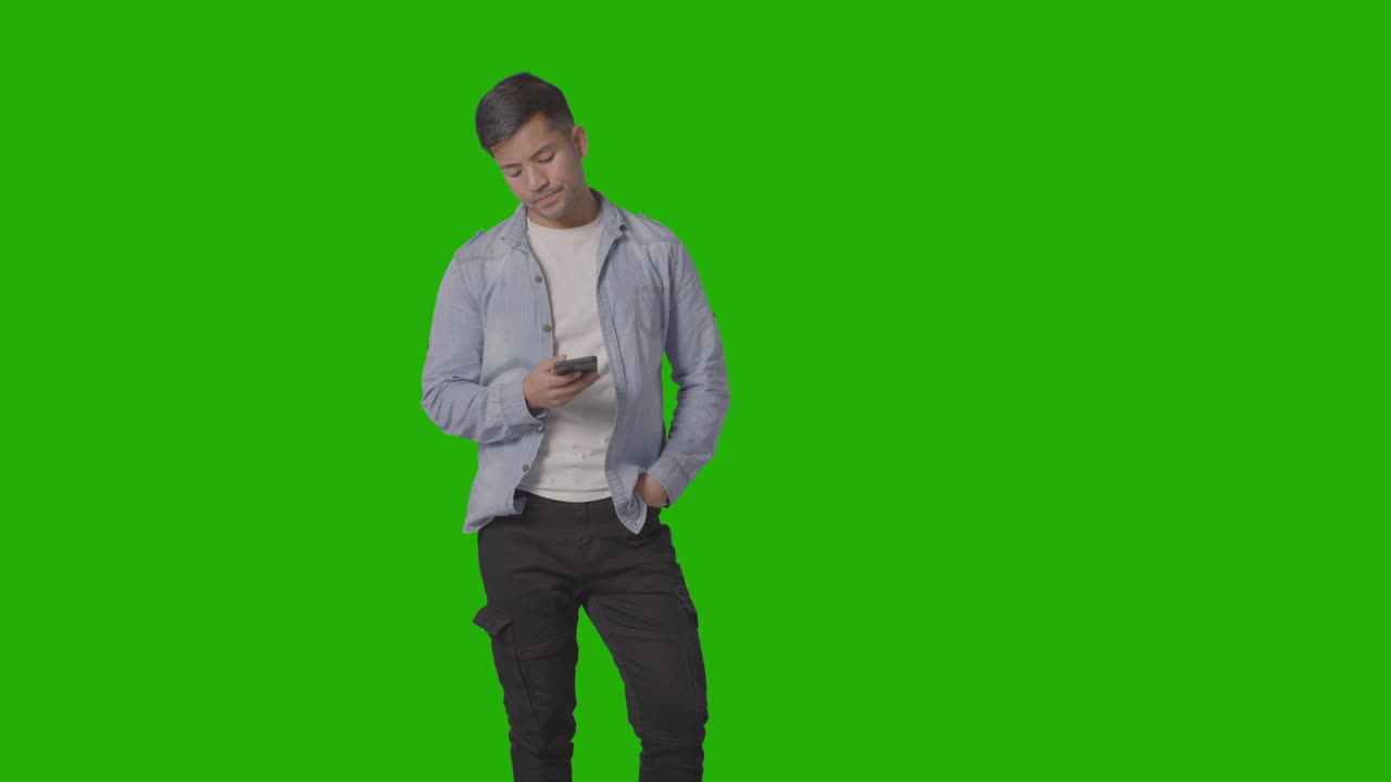 студийный снимок непринужденно одетого молодого человека, проверяющего мобильный телефон на фоне зеленого экрана 3