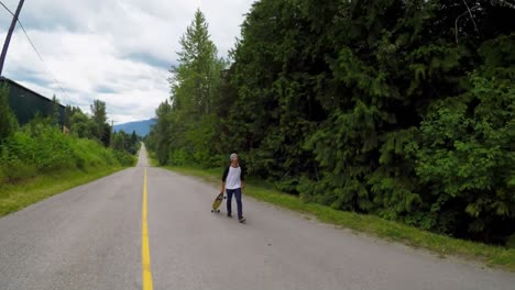 man with skateboard walking on rural road 4k