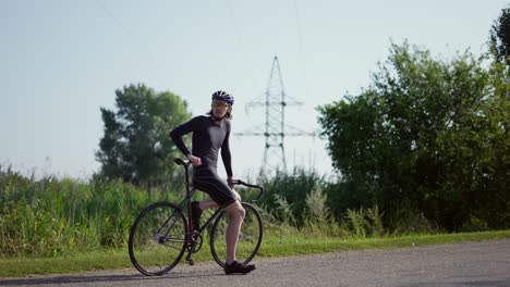 porträt eines radfahrers auf der leeren straße, der auf seinem fahrrad ruht