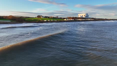 marea vespertina: imagen aérea baja de olas y surfistas y el resplandor del atardecer en la playa de thorntonloch, costa escocesa, dunbar, escocia, reino unido