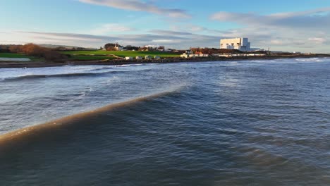 evening tide: low aerial of waves and surfers and the sunset glow at thorntonloch beach, scottish coast, dunbar, scotland, united kingdom