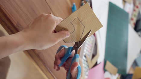 close up of hand using scissors cut a house on cardboard