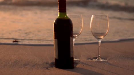 botella de vino rojo y vasos en la arena de la playa