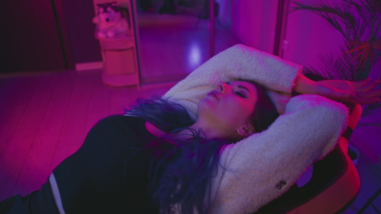 programmer takes nap reclined in gaming chair in vibrant neon lit studio surrounded by monitors drum set and tech equipment, recharging during coding session, eyes closed in peaceful rest