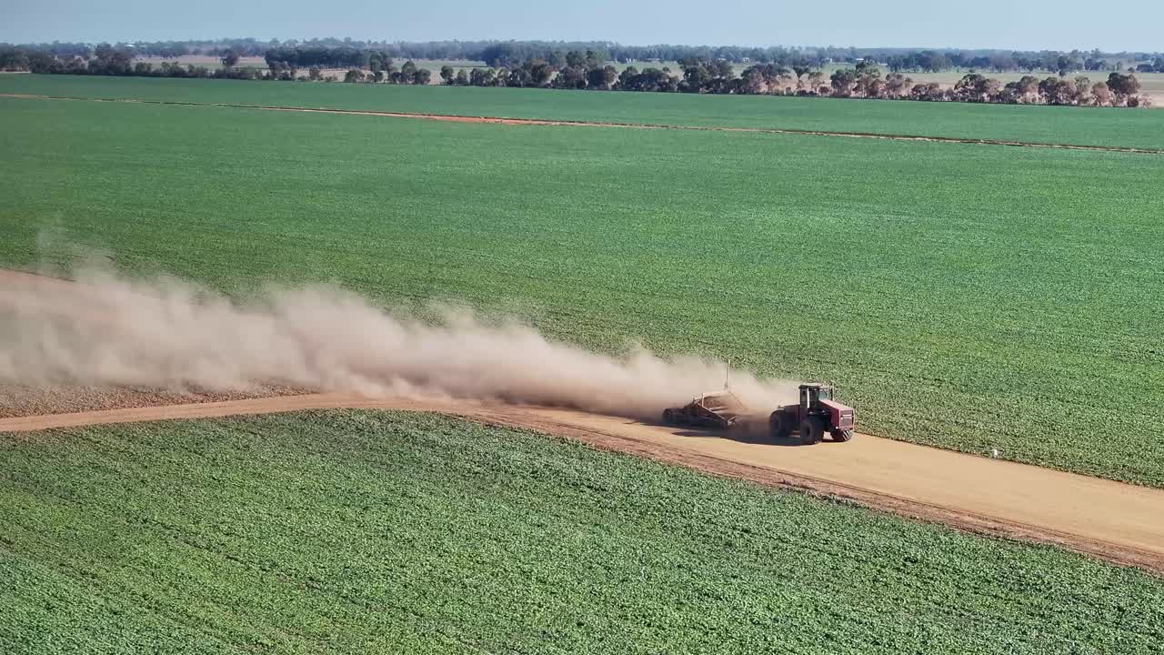 Nuvole di polvere si alzano da un trattore e una piccola livellatrice stradale su una strada agricola sterrata
