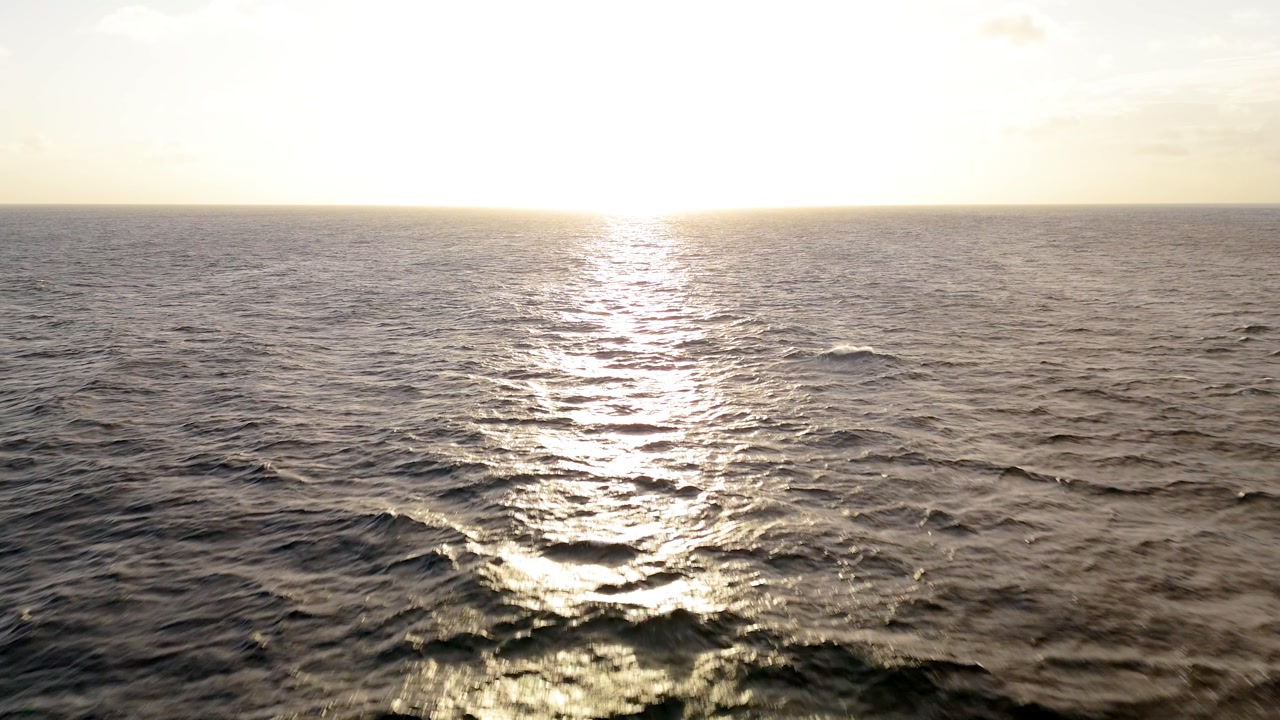 Drone seascape facing the sun with shimmering reflections on calm waves during sunset off Curacao.