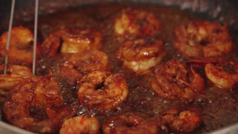 delicious seafood cooking scene with chef using tongs to flip the prawns, coating shrimps with sweet paprika sauce, simmering on hot shallow frying pan, close up shot