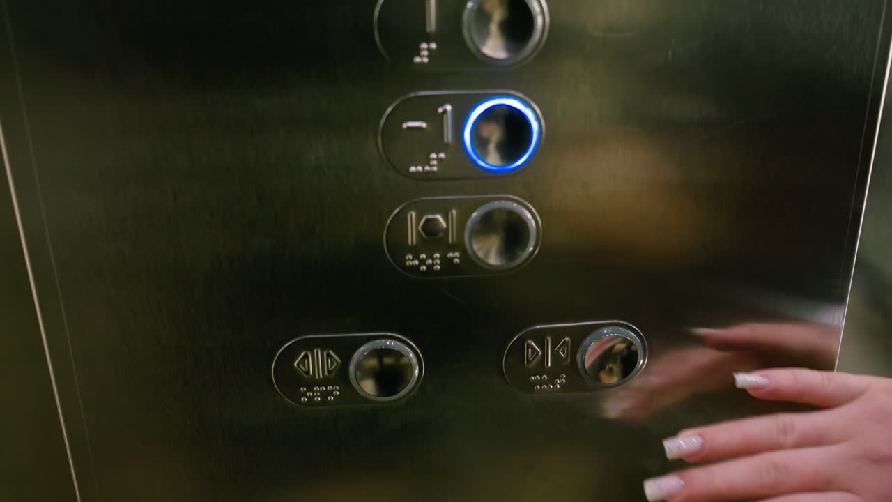 close up hand with long manicured nails reaching to press button on elevator control panel with stainless steel surface and braille markings, reflecting soft ambient light in modern indoor setting