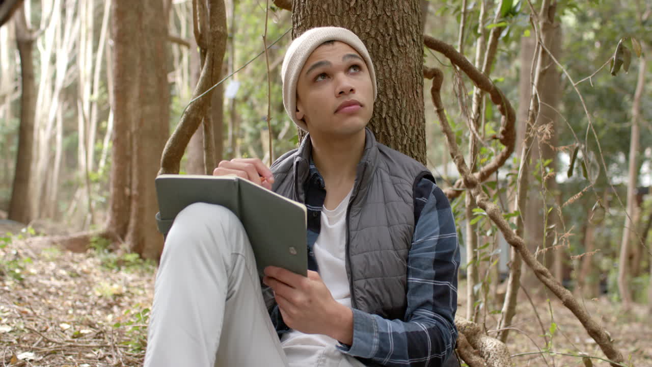 Young man in forest writing in notebook, reflecting on nature's beauty
