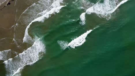 top view of beautiful green ocean waves crashing onto sandy beach