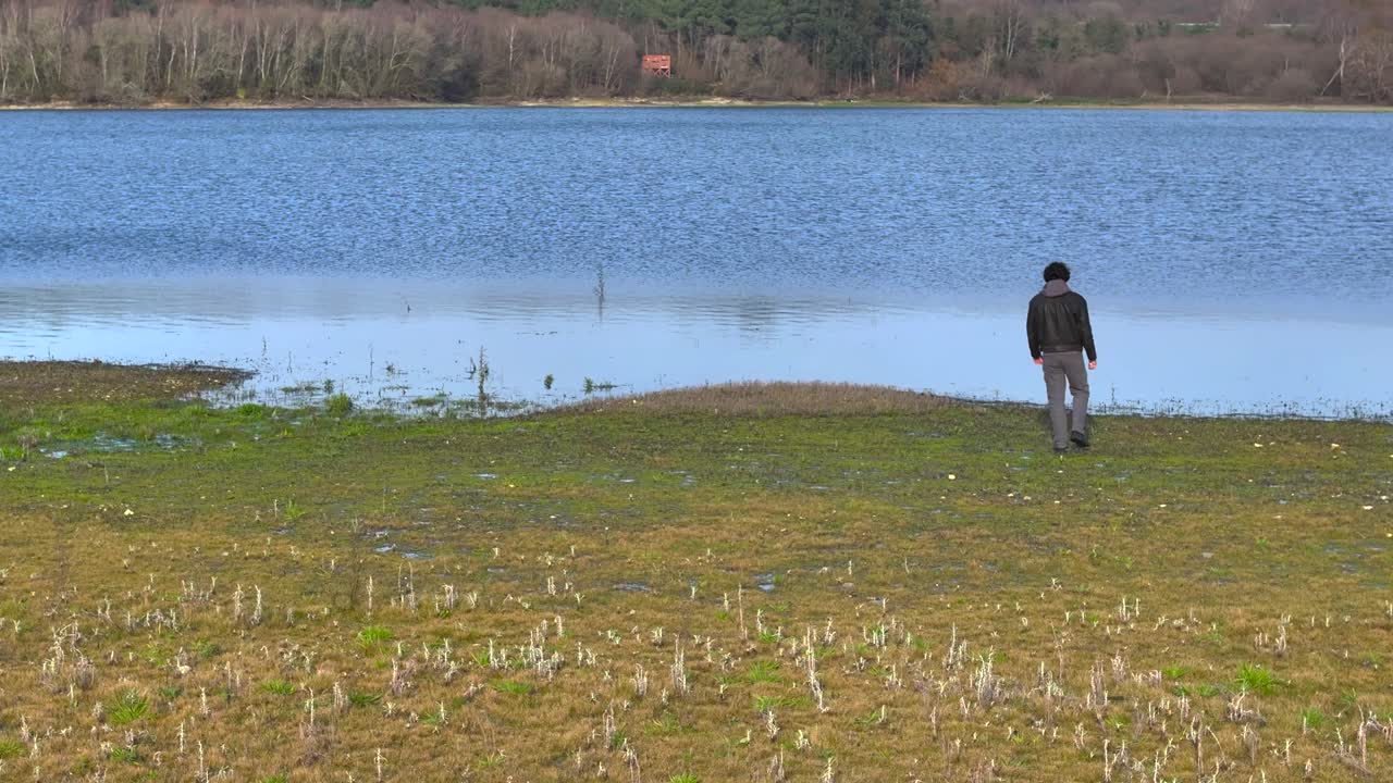 un hombre está caminando solo hacia un lago tranquilo durante el día