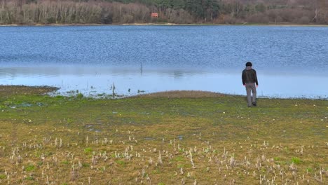 un hombre está caminando solo hacia un lago tranquilo durante el día