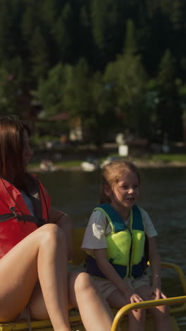 glad young mother and daughter sit in catamaran. smiling woman and girl talk relaxing on lake on sunny day slow motion. family summer vacation