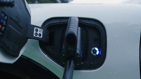 Recharging-Battery-of-Electric-Vehicle-at-Charging-Station,-Cable-and-Plug-Connected-to-Socket-on-Car,-Close-Up