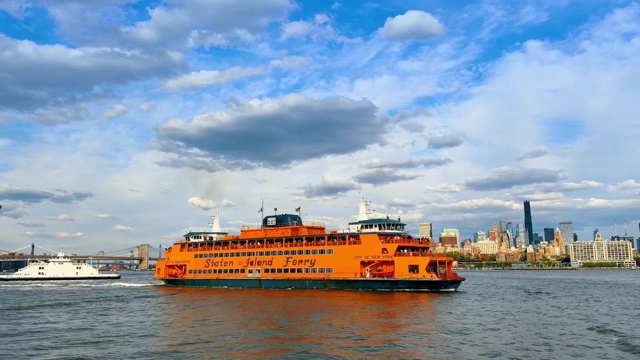 New York, USA, 1. maj 2026: Ikonisk orange Staten Island Færge sejler i New York. Stort orange Staten Island Færgefartøj på vandet med Manhattans skyline og bro i det fjerne.