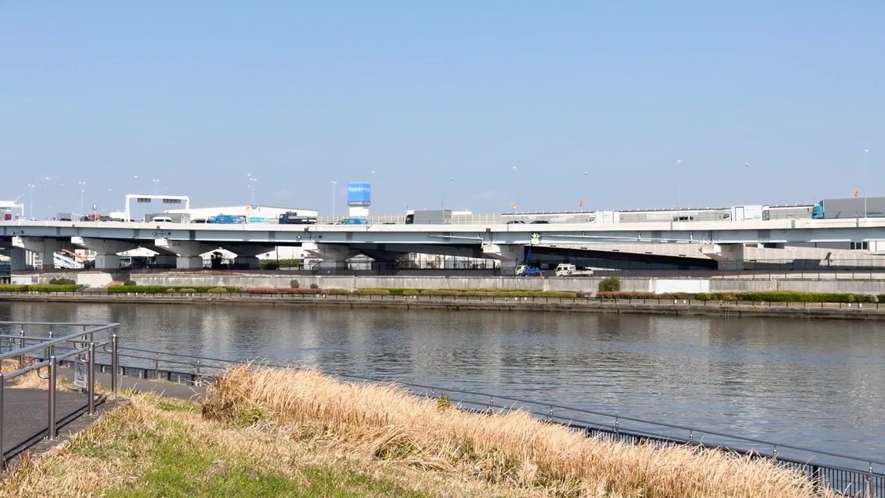 澄み切った青空の下、穏やかな川の上に架かる多層の高速道路橋を車両が渡っている。