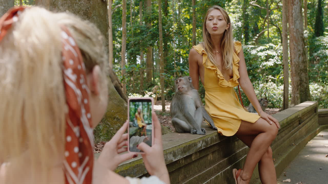 mujer turista usando un teléfono inteligente tomando una foto de su amiga posando con un mono en el zoológico de vida silvestre divirtiéndose compartiendo la aventura de viaje