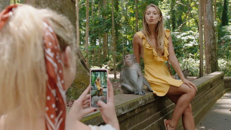 tourist woman using smartphone taking photo of friend posing with monkey in wildlife zoo having fun sharing travel adventure