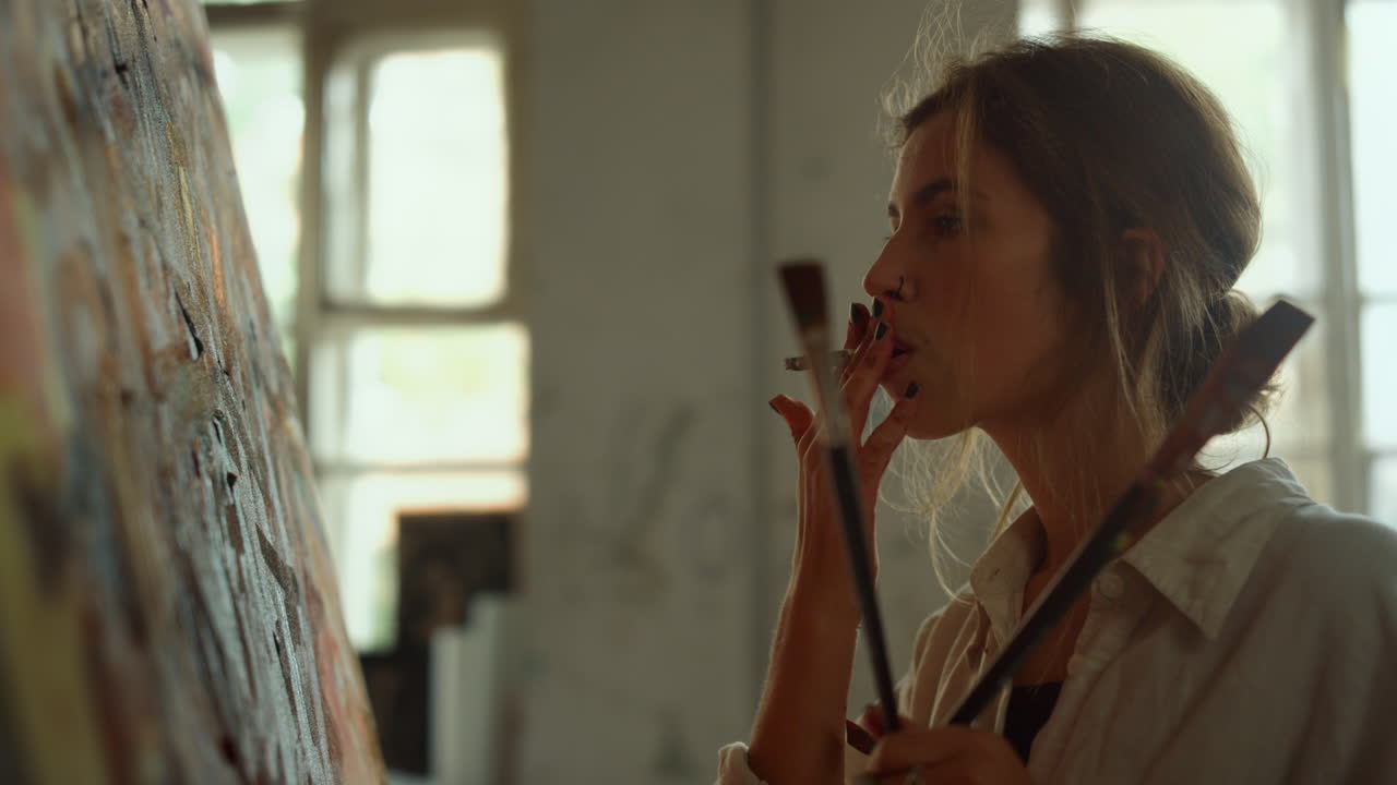 실내에서 담배를 들고 있는 재능있는 여성. 예술 스튜디오에서 휴식을 취하는 피곤한 예술가.