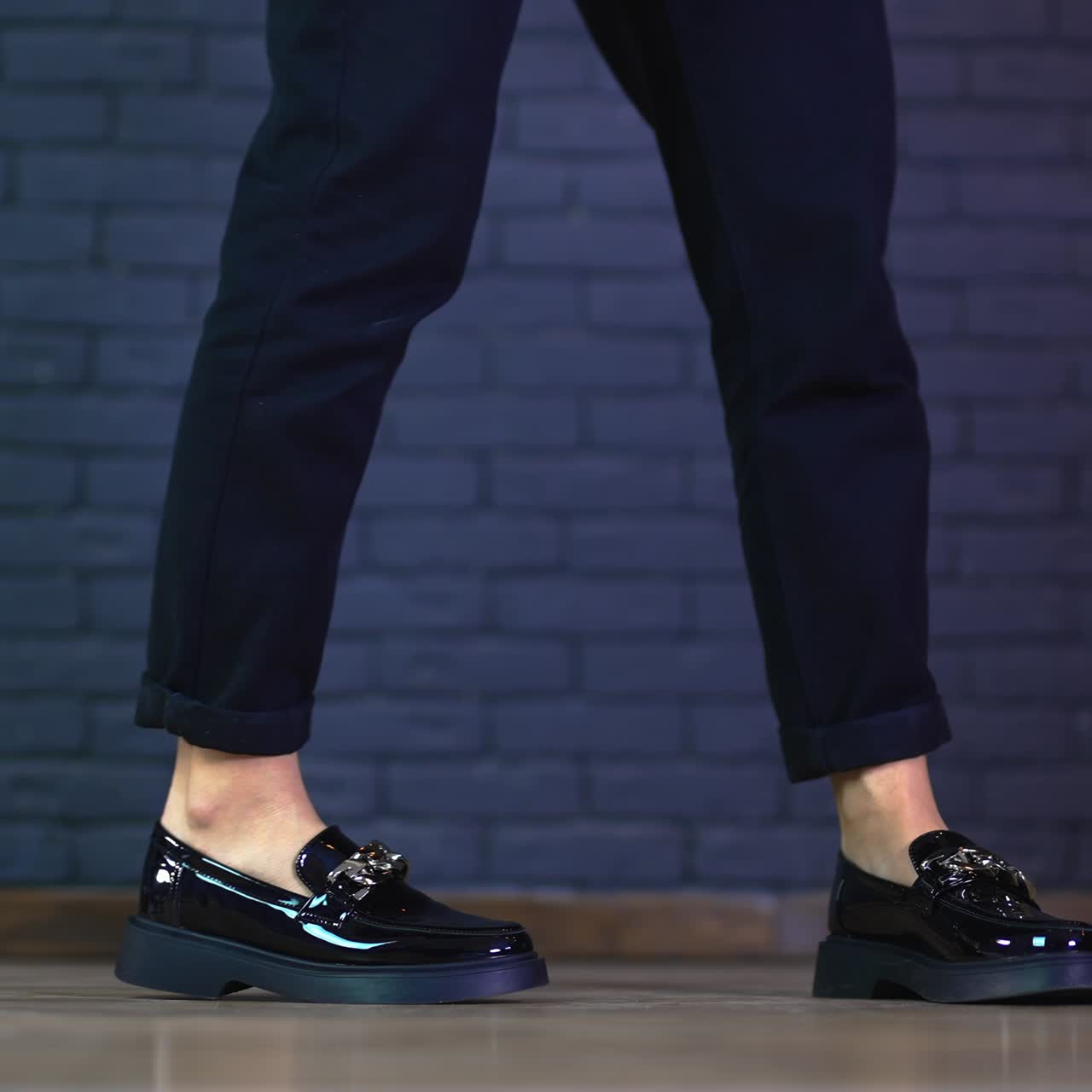 Girl in black jeans demonstrating modern massive shoes with silver chain decoration. Grey brick wall background