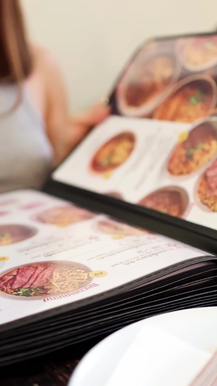 En kvinde bladrer i en farverig madmenu ved et restaurantbord, under blød indendørs belysning, med fokus på nordthailandske retter.