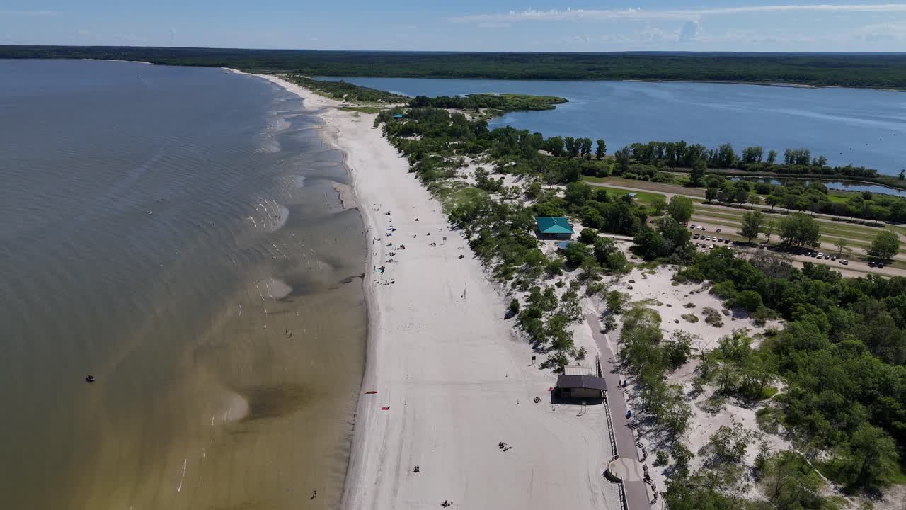 Aerial drone timelapse from far over Lake Winnipeg looking east at Grand Beach, Manitoba. Summer day with people on the beach, sandy shoreline, lagoon, and boreal forest in the background