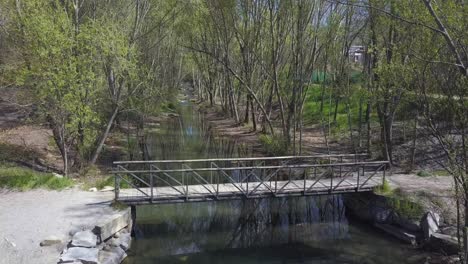 Wooden Bridge Over Calm River With Trees Growing In Riverbank At Summer. - aerial
