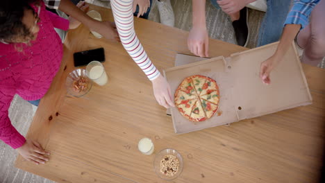 Happy-diverse-group-of-teenage-friends-sitting-on-couch-and-sharing-pizza-at-home,-slow-motion