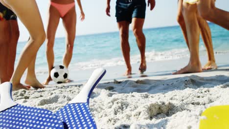 Low-section-of-friends-playing-football-at-beach