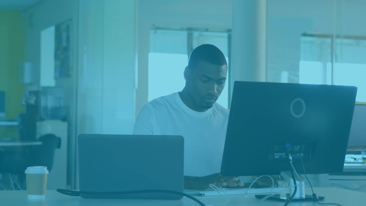 Animation of graphical clouds and computer icons over african american businessman using computer